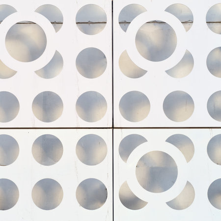 Abstract pattern of circular cutouts on white metal panels with gray background. Geometric design...