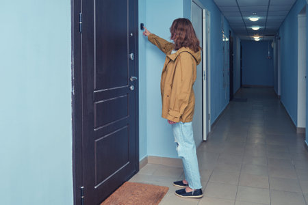 Person ringing doorbell in a residential hallway. Indoor photography of a woman wearing a yellow...