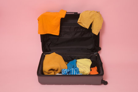 Open black suitcase with colorful clothes on studio pink background.の写真素材