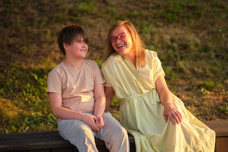 An affectionate portrait of a woman and her teenage son, both smiling with happiness against a lush...