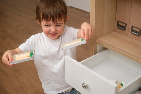 A child boy is holding a matchstick, which is highly flammable and risky. The baby is dangerously playing with a flame inside the house. Kid aged 3 years (three year old boy)の写真素材