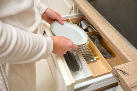Person placing a plate into a kitchen drawer with organized cutlery and utensils. Indoor kitchen organization concept for storage and home design.の写真素材