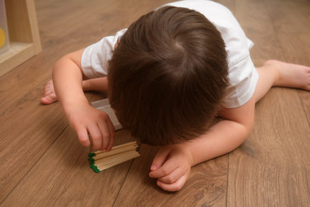 A toddler baby curiosity about matches can easily lead to a fire at home. The child boy lights a match indoors, creating a dangerous situation. Kid aged 3 years (three year old boy)の写真素材