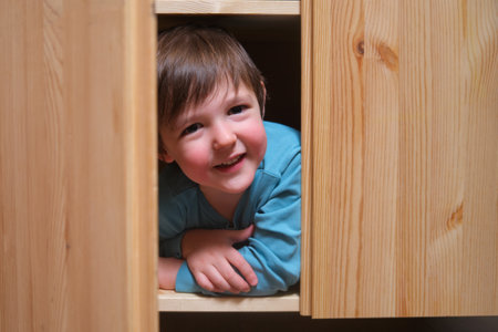 The child is tucked away inside the wardrobe, enjoying a playful game of hide-and-seek. Little baby boy is hiding happily inside the wooden cabinet, his smile peeking through the door. Kid aged 3 yearsの写真素材