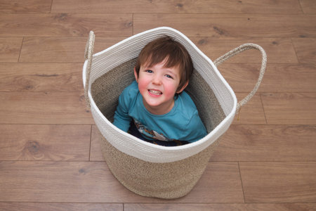 The little baby boy is tucked away in the woven basket, his eyes sparkling with mischief. The child hides playfully inside the basket, his face full of happiness and fun. Kid aged 3 yearsの写真素材