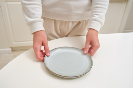 Person holding an empty ceramic plate on a white table. Close-up photography for design and printの写真素材