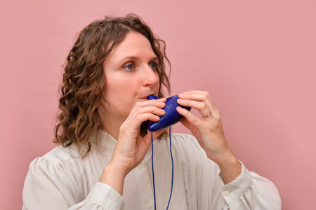 Woman playing blue ocarina against pink background. Studio portrait of musician holding a ceramic wind instrument. Music performance concept for design and print.の写真素材
