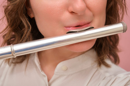 Close-up of woman playing a silver flute. Studio portrait on a pink background. Music and performance concept.の写真素材