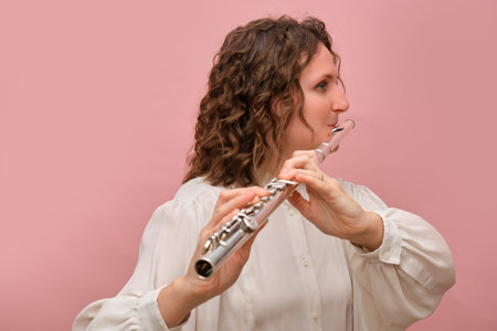 Female musician playing silver flute in white blouse. Studio portrait against pink background. Classical music and performance concept. Design for banner, poster, and header.の写真素材