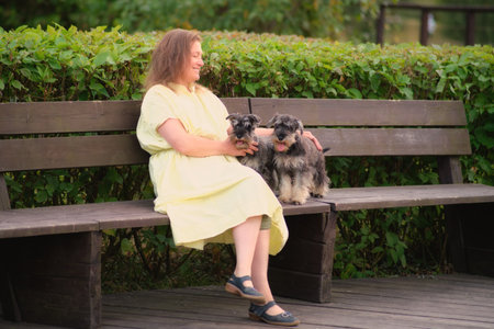 A person sits on a park bench with two miniature schnauzers, enjoying a peaceful moment in nature.の写真素材