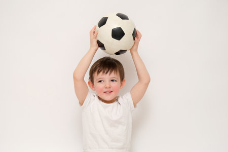 Boy holding a soccer ball over his head on a white background. Studio portrait photography. Sports and children concept. Kid aged three (three-year-old)の写真素材