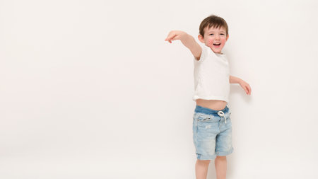 Smiling boy in casual summer outfit pointing to the side. Studio portrait on white background. Child lifestyle and playful childhood concept. Kid aged three (three-year-old)の写真素材