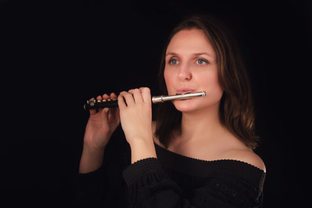 Woman holding and playing piccolo flute. Studio portrait of female flutist in black dress against...