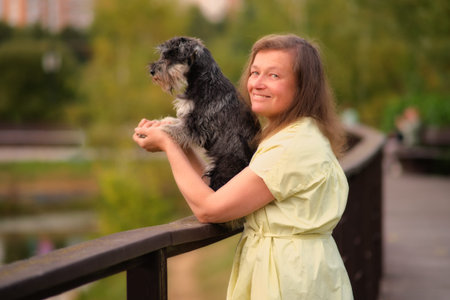 The woman takes her miniature schnauzer for an outdoor walk, enjoying the fresh breeze.