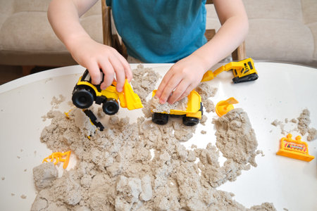 Childhood creativity flourishes as the child plays with sand at the table. Kid aged three years