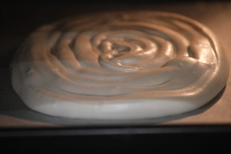 Swirled meringue mixture baking in the oven on parchment paper. Macro shot of dessert preparation....