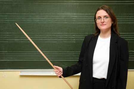 The smiling teacher in a jacket stands in front of the class, teaching students with enthusiasm. A person devoted to education is standing by the board, helping students learn new things.の写真素材