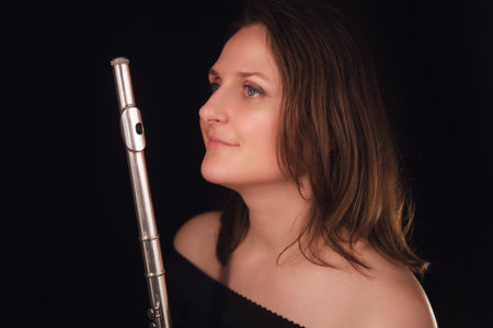 Woman holding flute against dark background. Studio photography of musician and performer.の写真素材