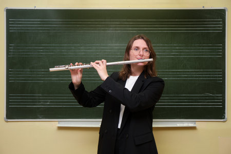 The smiling female teacher, a skilled flutist, stands by the blackboard in her classroom, happily playing a classic melody on her flute while her elementary students watch in awe.の写真素材
