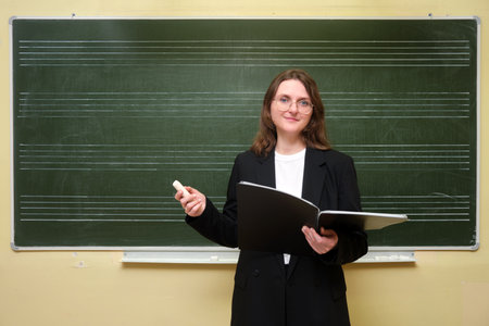 The smiling woman, a school teacher, is standing near the chalkboard, bringing happiness to the classroom. A person dedicated to education is standing in the classroom, happily writing on chalkboard.の写真素材