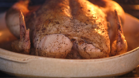Whole roasted chicken with seasoning in a ceramic baking dish inside an oven. Close-up food photography of homemade poultry meal preparationの写真素材