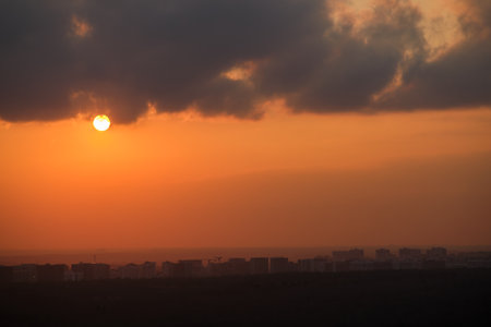 Sunset over city skyline with dark clouds. Urban landscape with orange sky and setting sun. Cityscape photography with copy space.の写真素材
