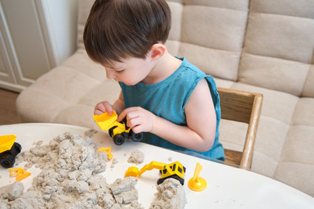 A child is playing with kinetic sand on the table in the cozy living room. Kid aged three yearsの写真素材