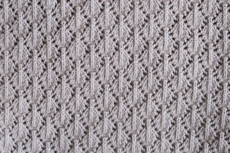 Knitted fabric with symmetrical lace pattern in light gray color. Close-up texture of handmade...