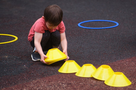 Young child organizing yellow cones during outdoor activity, promoting early learning, coordination, and physical development on the playground. A child aged 3 yearsの写真素材