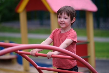 Caucasian boy playing on a red jungle gym. Happy kid enjoying outdoor activity at a playground. Childhood and summer concept. A child aged 3 yearsの写真素材