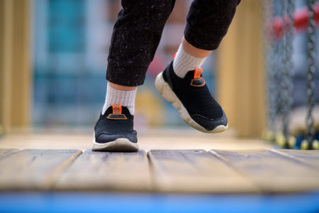Kid's legs and feet in sneakers on playground background. Child legs walking on wooden planks....