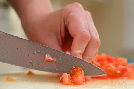 Macro photo of a person slicing a ripe tomato with a kitchen knife on a cutting board, showing detailed food preparation.の写真素材