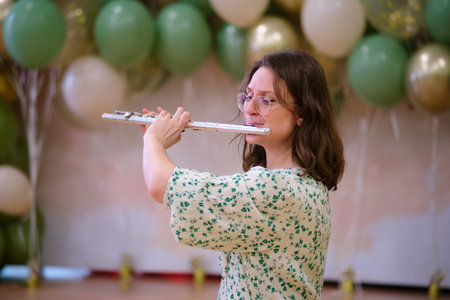 A woman in a floral dress plays the flute at a cheerful celebration, standing in front of colorful party balloons.の写真素材