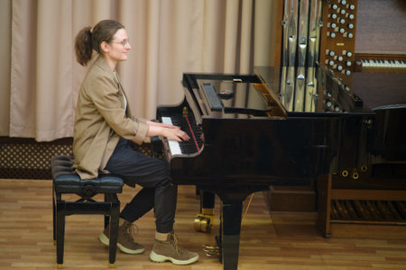 Casually dressed woman plays a grand piano in a professional music room, possibly practicing or recording classical music.の写真素材