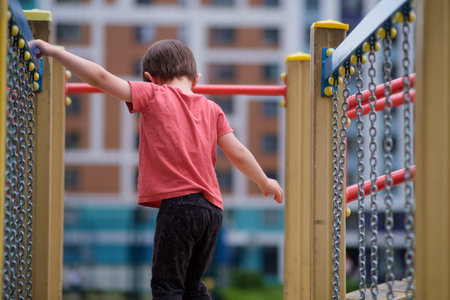 Little kid playing on bright playground equipment outdoors, exploring chains and beams. Child...