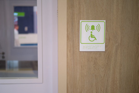 Green handicap accessible restroom sign with braille and emergency bell icon on a wooden door. Accessibility concept.の写真素材