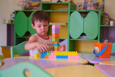 Little boy child playing with colorful building block toy at kindergarten table creating a tower....