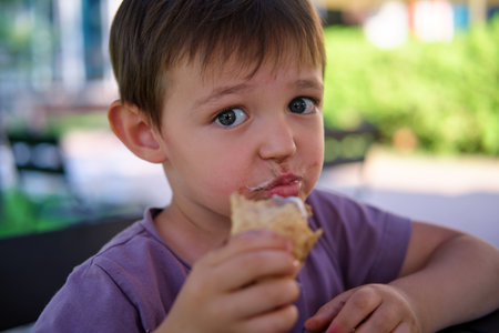 Happy boy eating delicious ice cream cone on sunny summer day. Child enjoying sweet dessert. Snack time for kid. A child aged four years.の写真素材