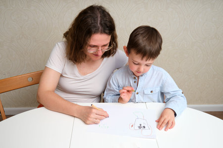 Woman draws with her son at table, teaching child creative skills. Family leisure time and early...