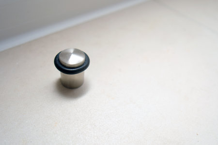 Metal door stop with black rubber ring on light floor. Modern home hardware protection. Interior floor accessory for domestic property.の写真素材