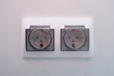Double electric power socket with clear protective cover on a white wall. Home electrical wiring and...