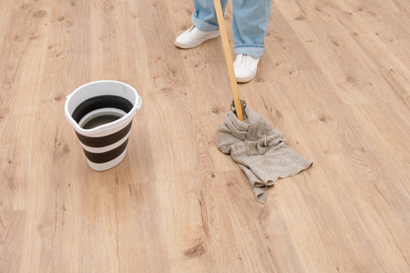Woman in blue jeans and white shoes mopping a light wood floor with a bucket of water. Home cleaning...