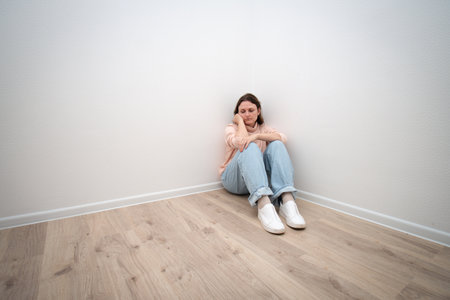Sad woman sitting alone in room corner with hands on face. Concept of depression, loneliness, mental health issue, domestic violence, isolation, and stress.の写真素材