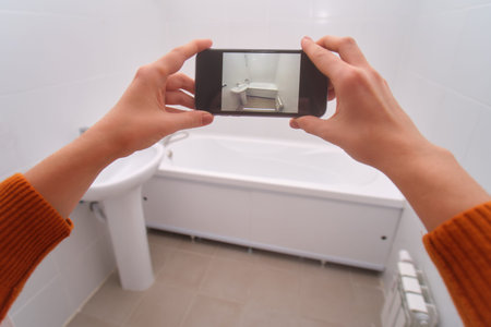 Woman holding smartphone taking picture of new white bathroom with modern sink and bathtub, renovation and interior design concept.の写真素材