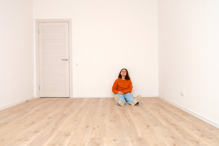 Woman sitting on floor in empty room thinking about renovation. New home, apartment buying, house warming, interior design concept.の写真素材