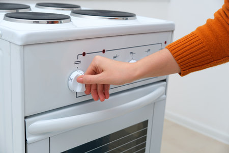 Woman hand turning kitchen stove knob for cooking. Appliance usage for preparing meal. Modern home electric cooker with oven.の写真素材