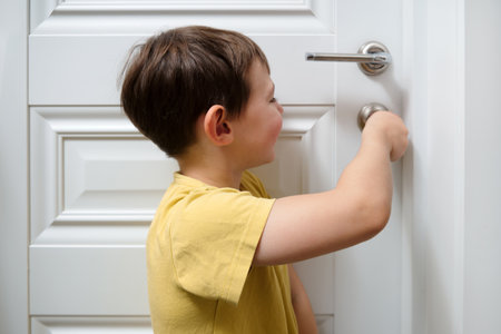 Little boy opening door while turning knob. Child learning to use doorknob. Curiosity and exploration in a home environment for early childhood development. Child aged 4 years (four years old)の写真素材