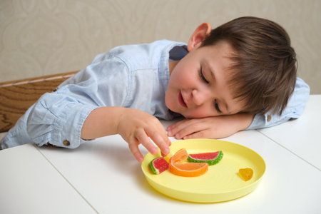 Boy reaching for candy on a yellow plate. Child enjoying sweet dessert, a moment of indulgence, concept depicting childhood and pleasure. A child aged 4 years (four years old)の写真素材
