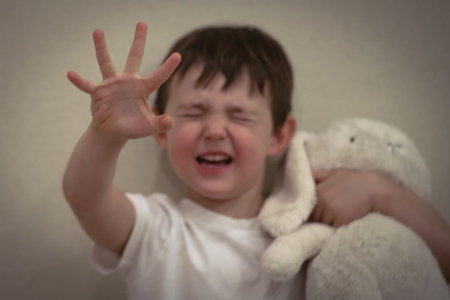 Scared little boy raising hand while holding a plush toy.