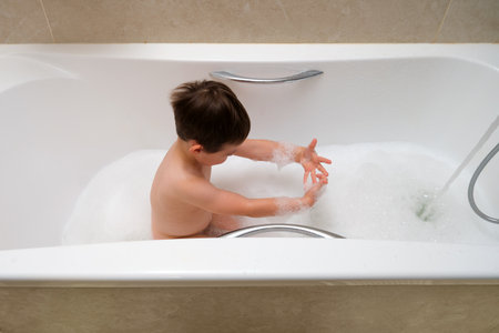 Child boy sitting in a bathtub full of bubbles, playing with foam during bath time, enjoying water and relaxation at home. Child aged 4 years (four years old)の写真素材